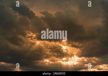 Dark threatening storm clouds filling the sky with powerful golden sunburst sunbeams breaking through the dramatic overcast atmosphere. Stock Photo