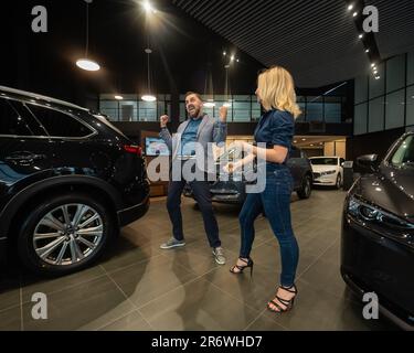 Happy married couple celebrating buying a car in a car showroom. Stock Photo