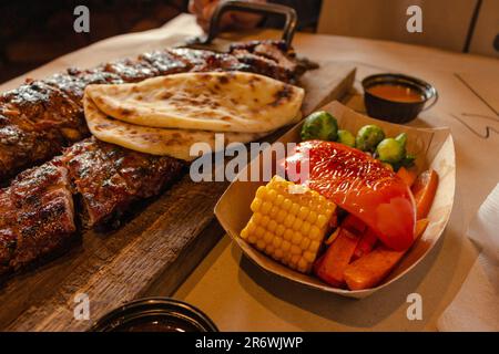 Grilled ribs with vegetables and bread. Smoked pork on wooden board and grilled vegetables. Dinner menu in restaurant. Medium roasted steak with corn. Stock Photo