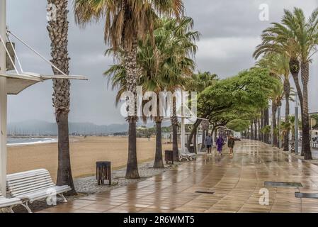 Three people walking on a rainy day along the promenade of Prat d'en Forès i Regueral Beach in Cambrils, Tarragona, golden coast, Catalonia, Spain. Stock Photo