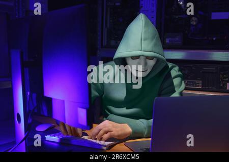 Hacker in mask working with computers in dark room. Cyber attack Stock Photo