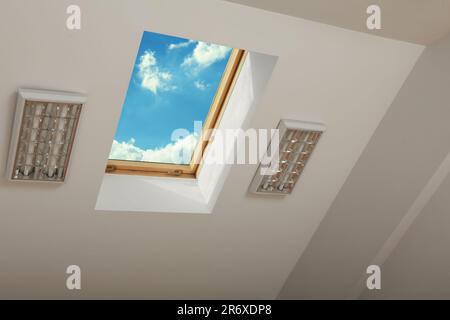 Skylight roof window and lamps on slanted ceiling in attic room, bottom view Stock Photo