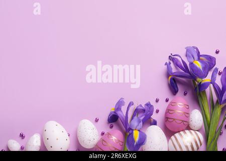 Flat lay composition with festively decorated Easter eggs and iris flowers on violet background. Space for text Stock Photo