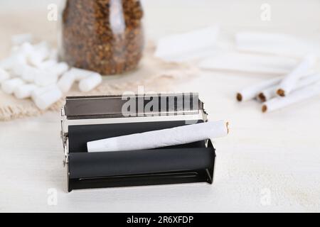 Manual roller with hand rolled tobacco cigarette on white wooden table, closeup Stock Photo