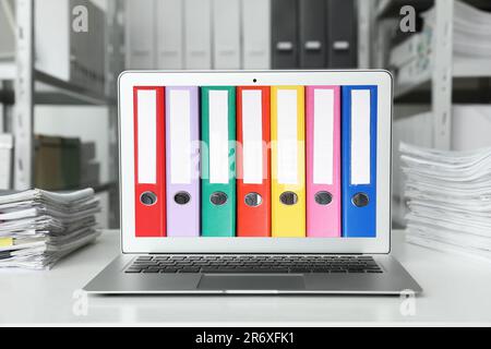 Store and organize information. Modern laptop with hardcover office folders on screen in archive room Stock Photo