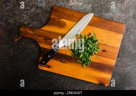 Chopped Basil with a Chef's Knife on a Wooden Cutting Board: Prepped Genovese basil leaves on a wood chopping board with a santoku knife Stock Photo
