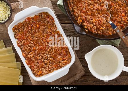 Preparing Lasagna in Rectangular Casserole Dish. Ragu or bolognese sauce on top of bechamel or white  sauce, ingredients on the side Stock Photo