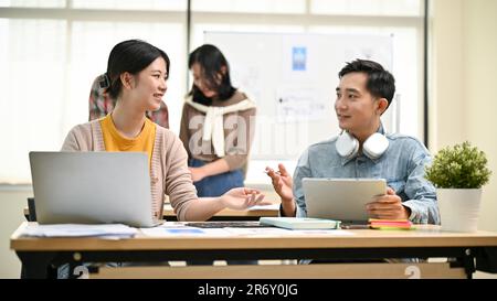 A beautiful and professional young Asian female worker in a tech company is discussing and sharing her ideas with a male colleague in the office. Busi Stock Photo