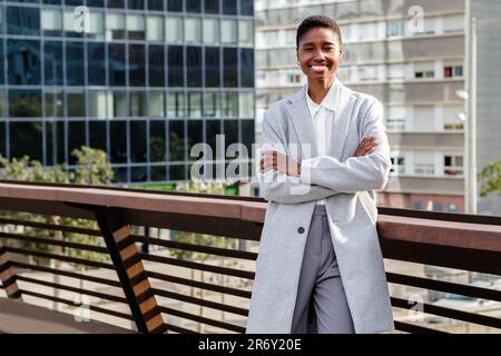 Cheerful african business woman looking at camera. She is crossing her arms and has offices buildings on the background Stock Photo