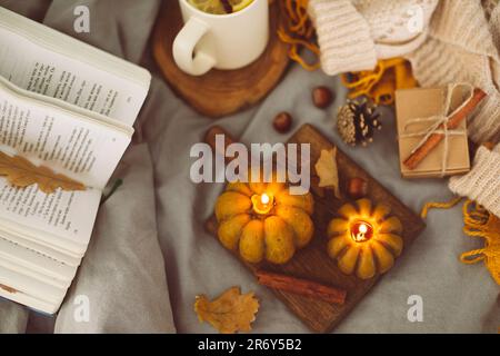 Top view on cozy mood composition with book, pumpkin candles, cup with hot tea and autumn decoration Stock Photo