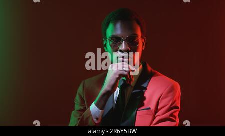 Pensive gentleman considering option. Green neon light confused perplexed business man in red tuxedo suit thinking on dark copy space background. Stock Photo