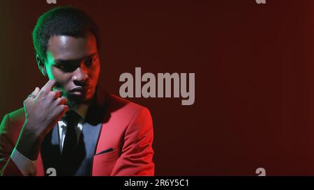 Man contemplation. Problem solution. Neon light puzzled concerned pensive gentleman in red tuxedo suit on dark empty space background. Stock Photo