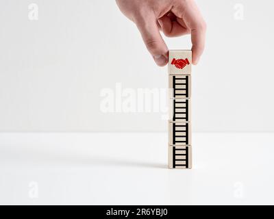 Business partnership deal. Achieving a business agreement. Mergers and acquisitions. Hand places a wooden cube with shaking hands icon on the cubes wi Stock Photo
