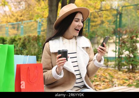 Special Promotion. Emotional young woman with smartphone and cup of drink in park Stock Photo