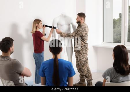 Soldier in military uniform teaching group of people how to apply medical tourniquet on mannequin indoors Stock Photo