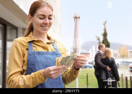 Happy waitress holding tips in outdoor cafe. Space for text Stock Photo