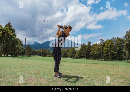Woman swinging club while playing golf at golf course, Bedugul, Bali, Indonesia Stock Photo
