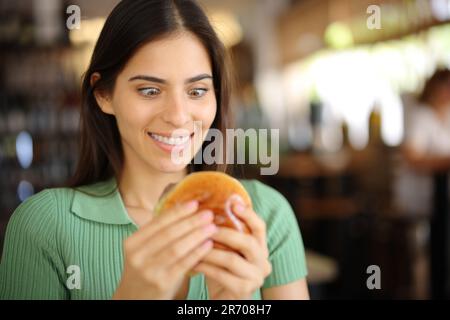 Glutton woman looking at burger in a bar interior Stock Photo