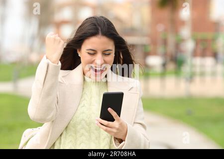Excited woman checking smart phone content walking in a park in winter Stock Photo