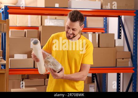 Post office worker wrapping parcel in stretch film indoors Stock Photo