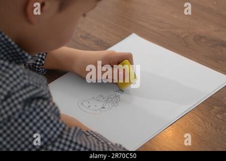 Little boy erasing mistake in his notebook at wooden desk, closeup Stock Photo
