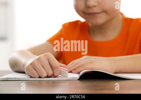 Little boy erasing mistake in his notebook at wooden desk, closeup Stock Photo