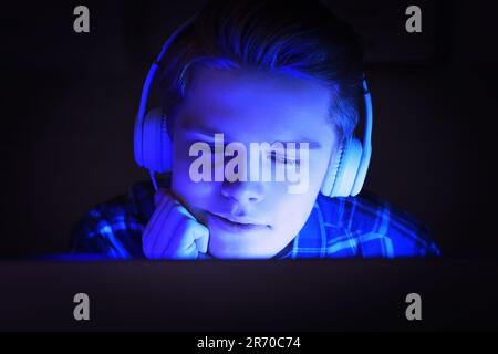 Internet addiction. Teenage boy in headphones using device at night. Toned in blue Stock Photo