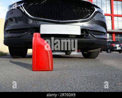 Red canister with motor oil near car on asphalt road, low angle view Stock Photo