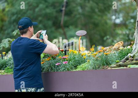 A mid 20s caucasian man in cap. Enjoy using smart phone taking picture of the beautiful flowers inside Flower Dome, Gardens by the Bay. Singapore. Stock Photo