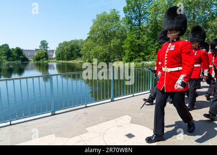 Soldiers crossing St James's Park bridge back to barracks following Colonel's review of Trooping the Colour. Buckingham Palace across lake Stock Photo