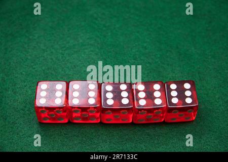 Five red dice with white dots in a row on a green felt surface displaying the numbers 1 to 6 Stock Photo