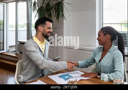 Young architect consulting project with client. Interior designer architecture expert making a deal with handshake after successful project and satisf Stock Photo