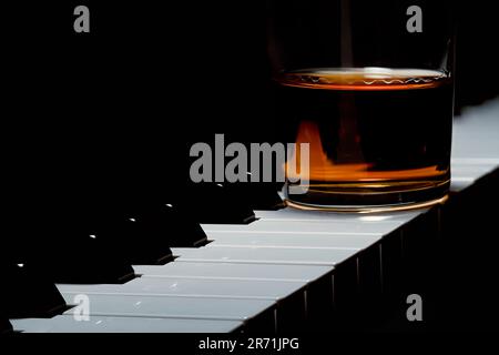 Piano keys with a glass of brown liquor, whiskey or cognac, sitting on the keys Stock Photo