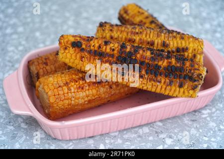Roasted corn cobs in a pink tray. Close up. Stock Photo
