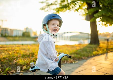 Funny toddler boy riding a baby scooter outdoors on summer day. Kid training balance on mini bike. Summer activities for small kids. Stock Photo