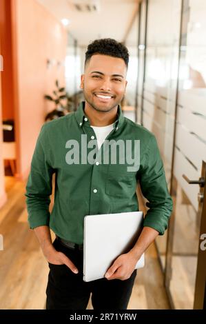 Successful young indian male entrepreneur, small business owner, male office employee in modern office, male student standing with laptop Stock Photo