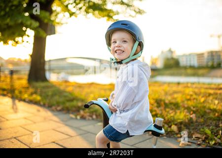 Funny toddler boy riding a baby scooter outdoors on summer day. Kid training balance on mini bike. Summer activities for small kids. Stock Photo