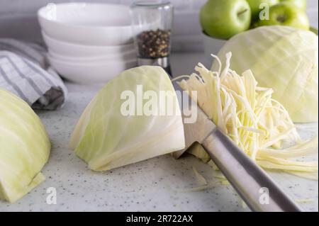 Chopped white cabbage on a cutting board on kitchen counter with chopper knife. Stock Photo
