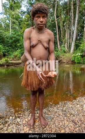 Woman of the Korowai tribe is standing on the banks of a forest river. Tribe of Korowai (Kombai, Kolufo). Stock Photo