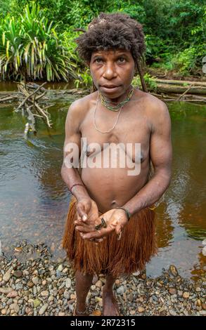 Woman of the Korowai tribe is standing on the banks of a forest river. Tribe of Korowai (Kombai, Kolufo). Stock Photo