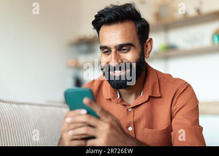 Portrait Of Indian Man Using Smartphone Sitting On Sofa Indoor Stock Photo