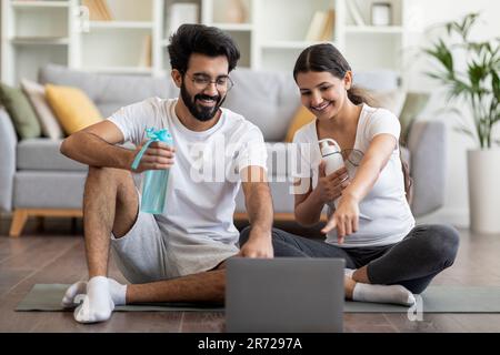 Happy Young Indian Couple Choosing Online Tutorials On Laptop For Home Training Stock Photo