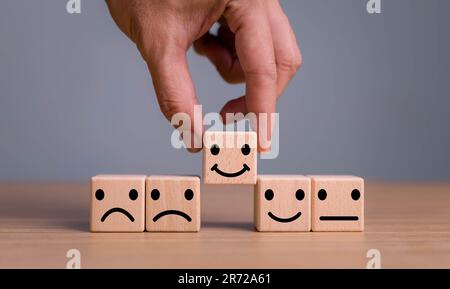 Hand putting virtual Emoji faces  print screen on wooden cube for Customer service evaluation concept. Stock Photo
