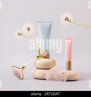 Facial anti-age massage for natural lifting and at home. Rose quartz facial roller and cosmetic bottle container on wooden stones with flower dandelio Stock Photo