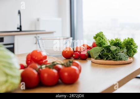 Variety of ripe vegetables and fresh greens being cleaned and ready for preparing salad on kitchen table indoors. Assorted mixture of ingredients adding dish more healthy nutrition and flavour. Stock Photo