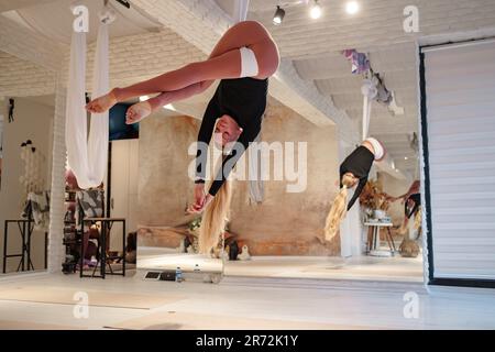 workshop of air yoga and stretching in yoga studio. women practices different inversion antigravity yoga with hammock. balance between mental and phys Stock Photo