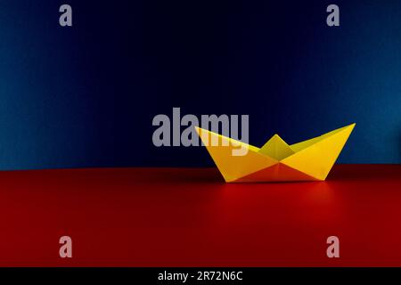 Folded yellow paper origami boat with a blue background and red base Stock Photo