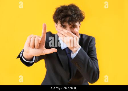 Laughing businessman showing loser gesture on yellow background Stock Photo