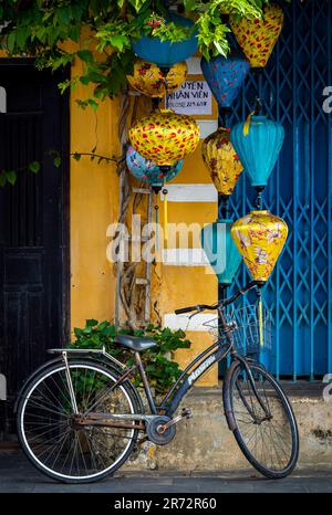 Hoi An, Vietnam, March 6th, 2023. Street view of a blue door with yellow lanterns and a bike in Hoi An old town. Stock Photo