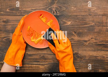 Female hands in rubber gloves washing dirty plate with sponge on wooden background Stock Photo